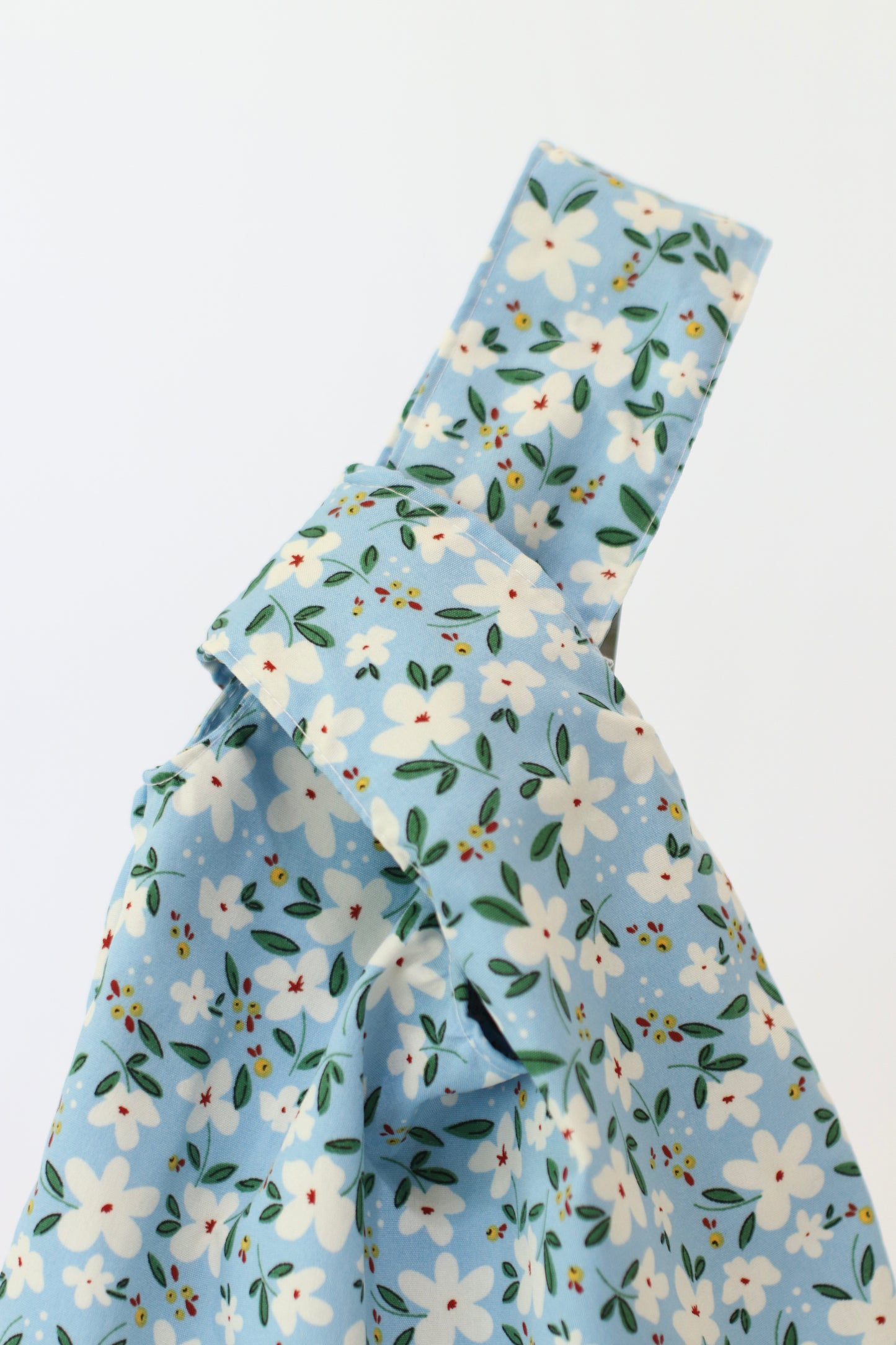 Knot Bag con estampado floral de flores blancas y hojas verdes sobre fondo celeste cielo.
