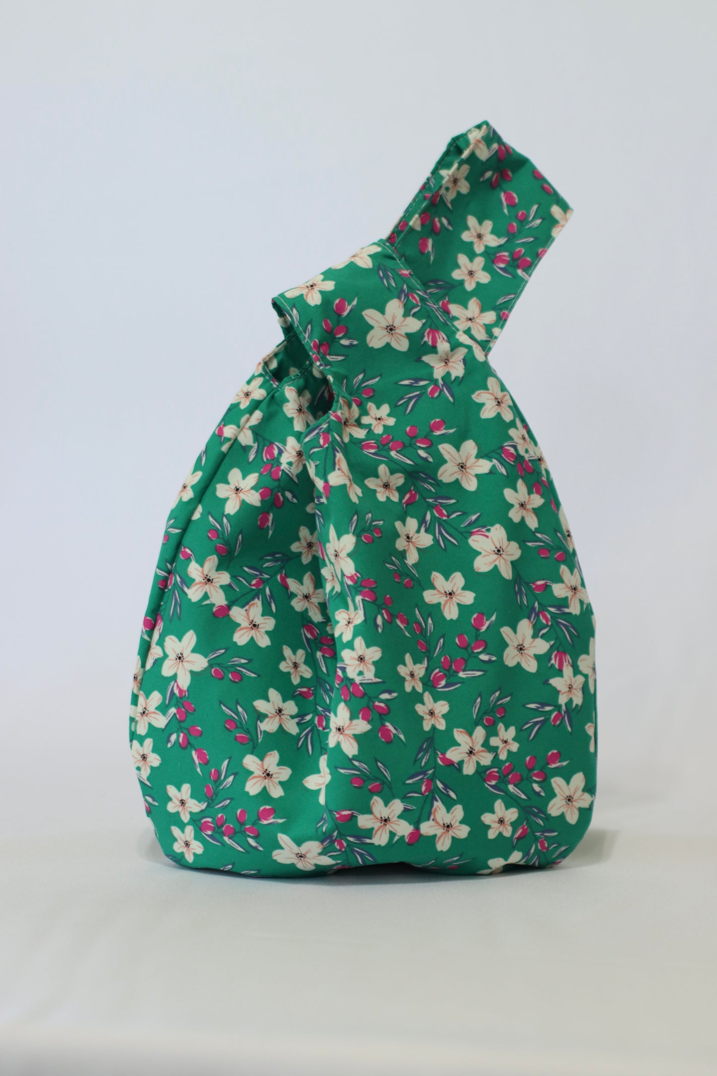Knot Bag con estampado floral de flores blancas y rojas sobre fondo verde, con diseño fresco y vibrante.