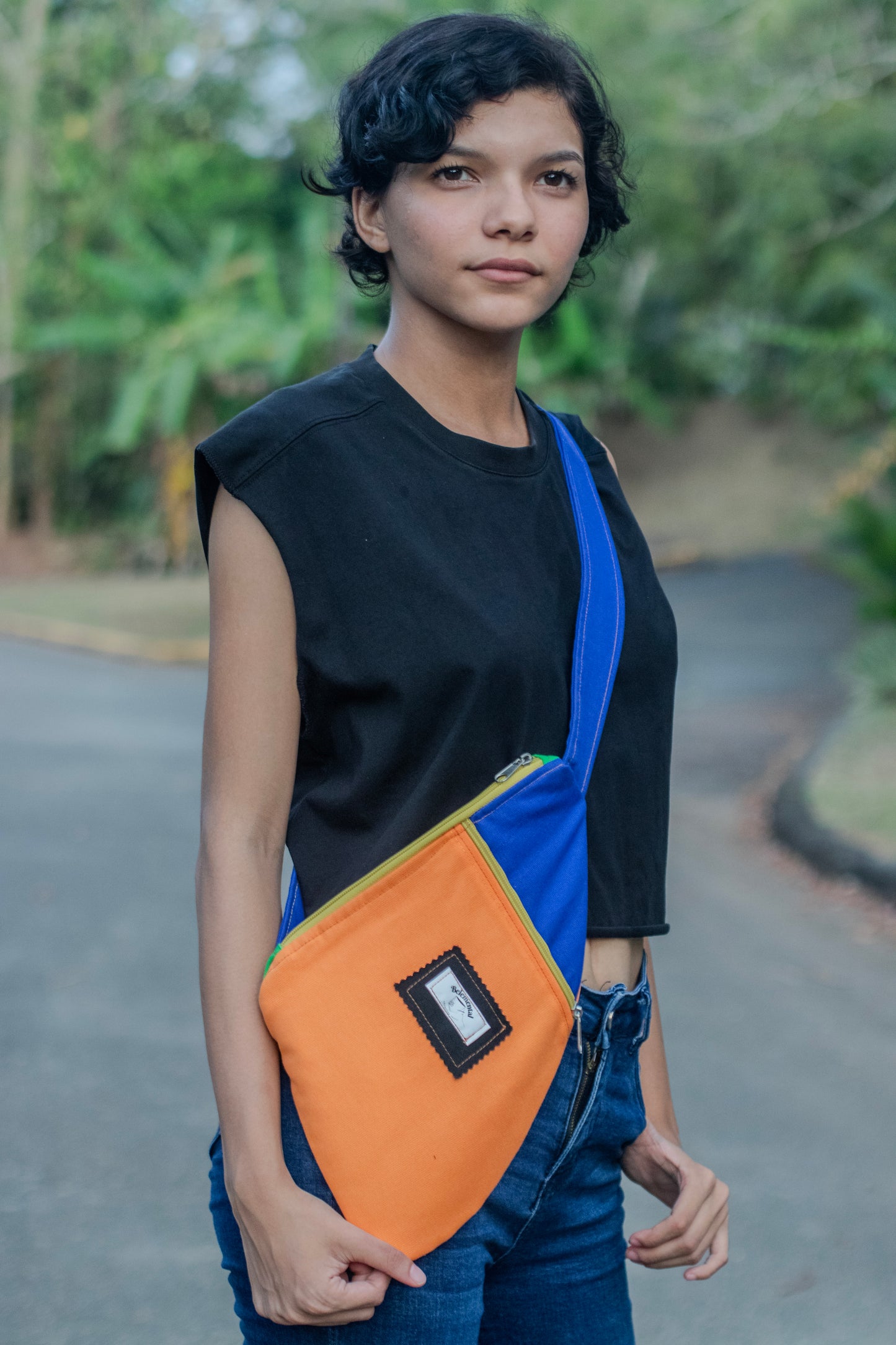 Mujer usando la Crossbody Bag en una combinación de colores naranja y azul, con detalles vibrantes en el cierre. La bolsa ofrece un diseño práctico y cómodo, perfecta para cualquier ocasión casual o activa.