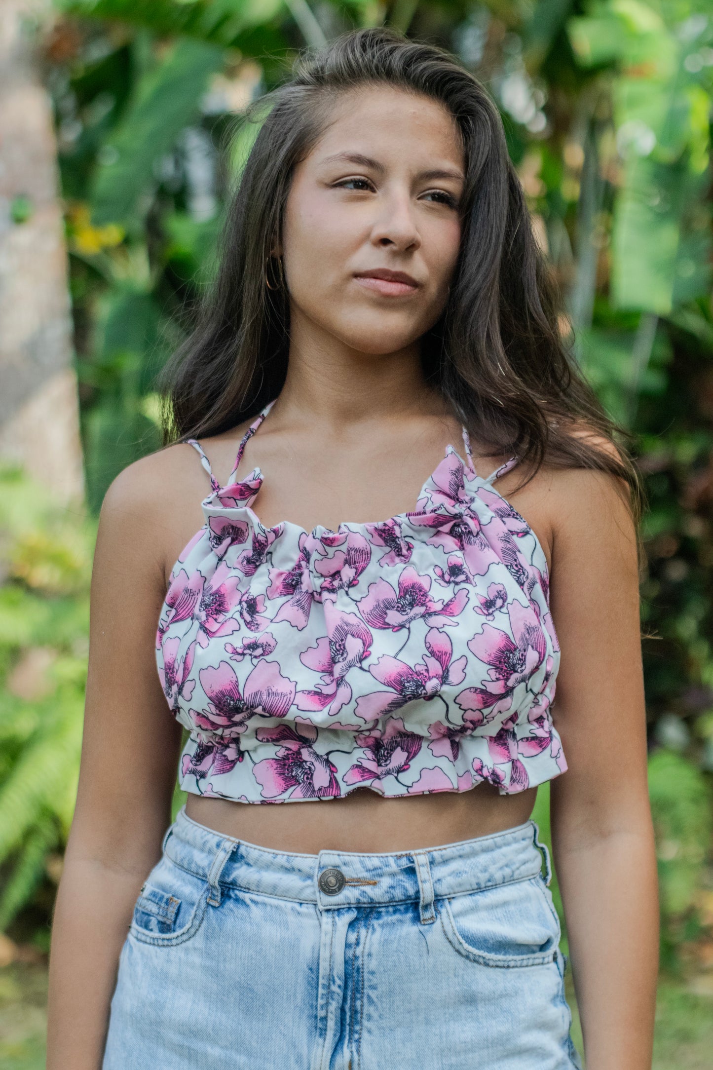 Mujer vistiendo un top fruncido y ajustable con un estampado floral delicado en tonos rosa sobre blanco, perfecto para complementar tu look casual de verano.
