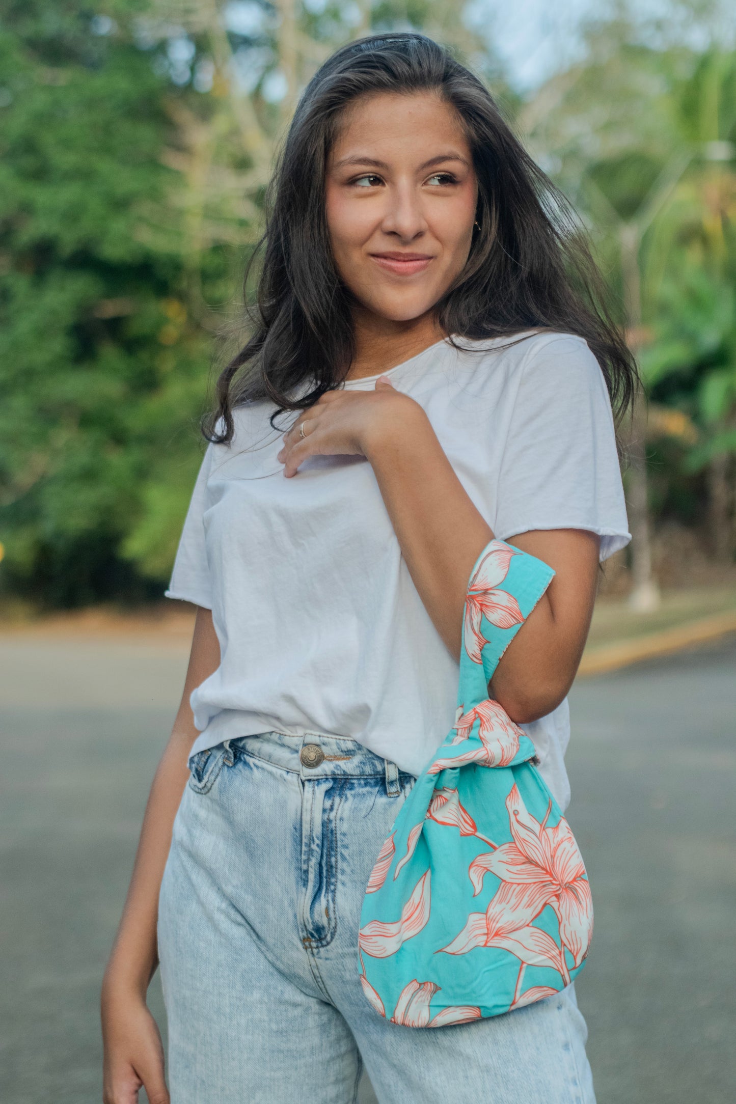 Modelo luce una Knot Bag de flores en tonos turquesa y coral, mientras posa con camiseta blanca.