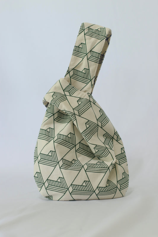 Knot Bag Belemental con un patrón geométrico en tonos beige y verde. La bolsa, hecha a mano con tela reciclada, muestra su característica forma de nudo en la parte superior.