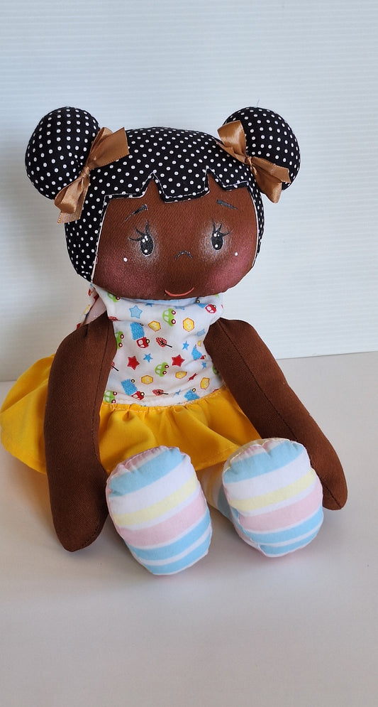 Muñeca de tela artesanal con cabello negro, vestido amarillo y detalles en blanco, decorada con lazos marrones.